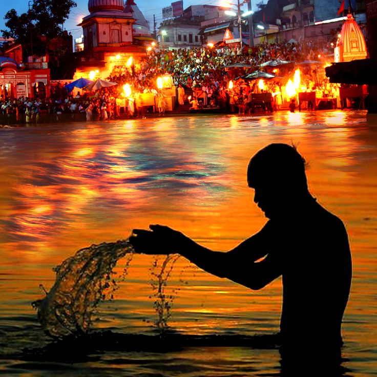 A devotee performing water offerings during Shradh 2024 at Pitru Paksha, with a large gathering in the background at a holy riverbank illuminated by ritual fires, symbolizing the significance of ancestral worship.