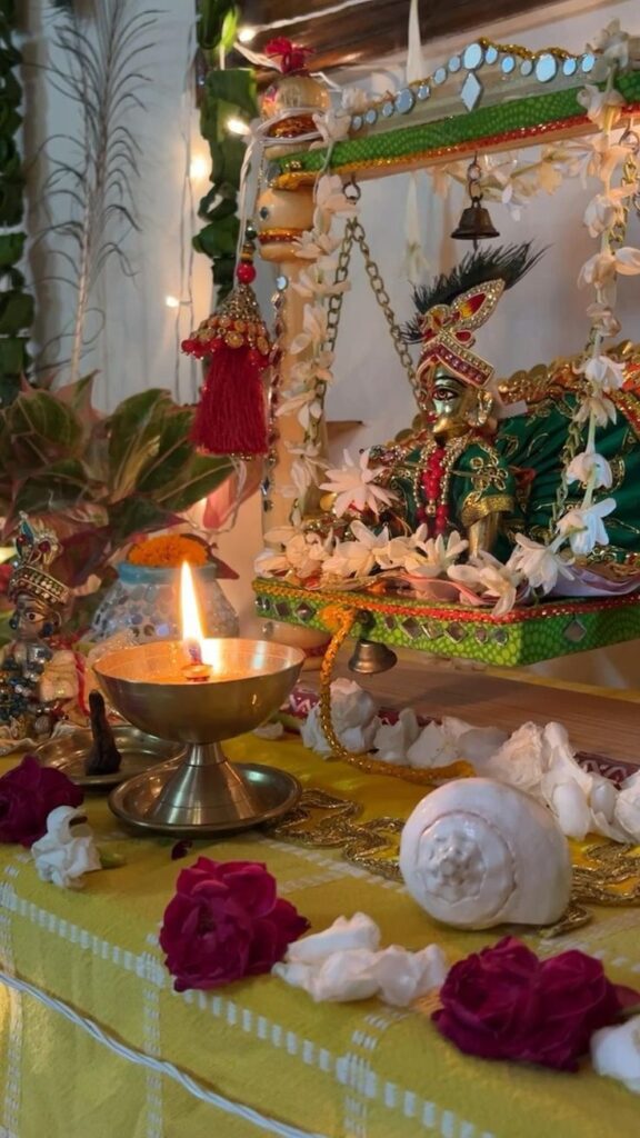 A beautifully adorned idol of Lord Krishna placed on a decorated swing, surrounded by flowers, a lit diya, and a conch shell, symbolizing the festive rituals of Krishna Janmashtami 2024. The vibrant setting reflects the devotional atmosphere of the celebration.